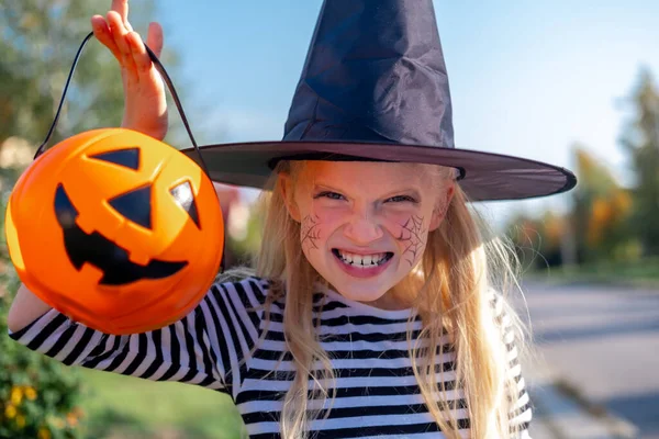 Halloween kids. Portrait Laughing girl in witch costume hat with pumpkin candy bucket on street — Stock Photo, Image