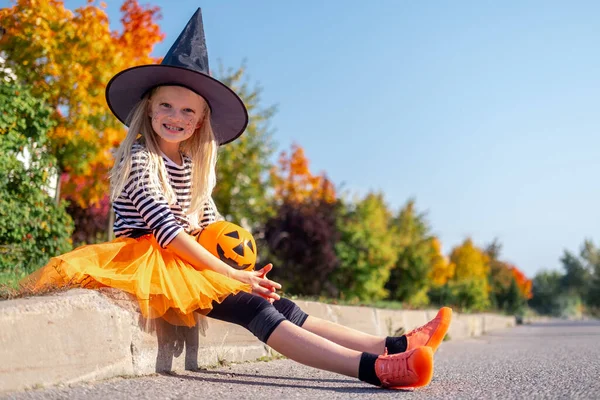 Cadılar Bayramı çocukları. Cadı şapkalı, elinde balkabağı şekeriyle gülümseyen kız portresi. Karnaval kostümlü komik çocuklar. — Stok fotoğraf