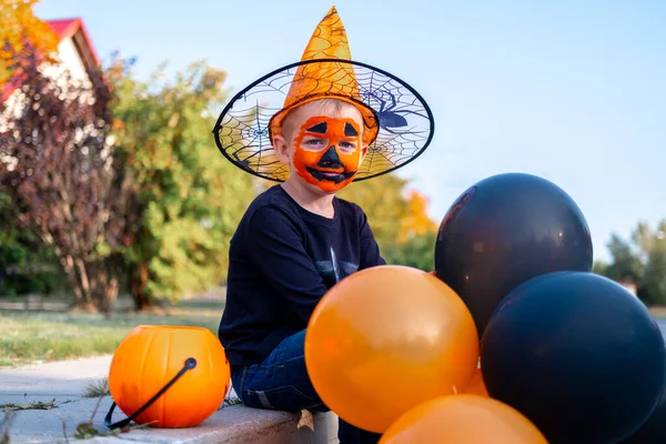 Niños de Halloween. Muchacho sonriente retrato en sombrero de bruja con globos naranjas y negras. Niños divertidos en trajes de carnaval al aire libre —  Fotos de Stock