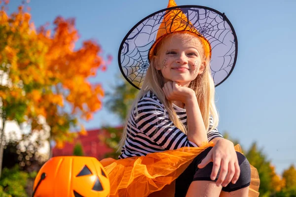 Bambini di Halloween. Ritratto ragazza sorridente con cappello da strega con secchio di caramelle alla zucca. Bambini divertenti in costumi di carnevale all'aperto — Foto Stock