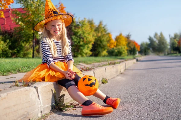 Niños de Halloween. chica sonriente en sombrero de bruja con cubo de caramelo de calabaza. Niños divertidos en trajes de carnaval al aire libre —  Fotos de Stock