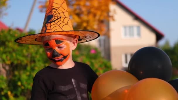 Halloween kinderen. jongen met pompoen masker in heksenkostuum hoed eet snoep van emmers die op straat zitten. Langzame beweging — Stockvideo