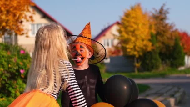 Langzame beweging. Halloween kinderen. Broer en zus in carnaval kostuums buiten. Jongen en meisje hebben plezier met oranje en zwarte ballonnen. — Stockvideo