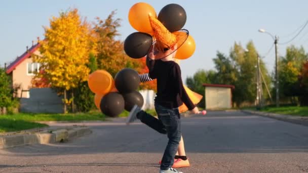 Slow motion. Halloween kids. Brother and sister in carnival costumes outdoors. Boy and girl having fun with orange and black balloons. — Stock Video