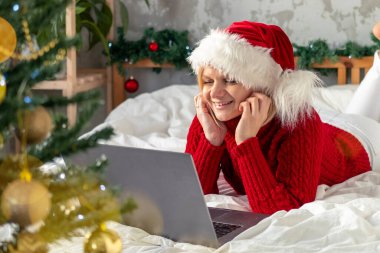 Noel alışverişi, iş ve eğitim. Evde bilgisayarlı Noel Baba şapkalı bir kadın var. Kış tatili satışları.
