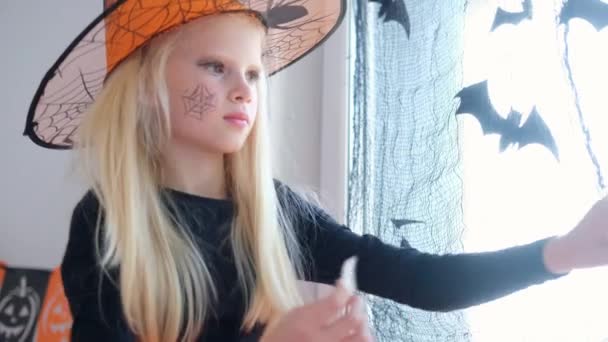 4k. gelukkig meisje in heks kostuum voorbereiding voor Halloween versieren venster in kamer door zwart vleermuizen — Stockvideo