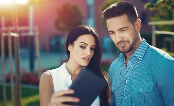 Young woman showing interesting news on tablet to man, outdoors