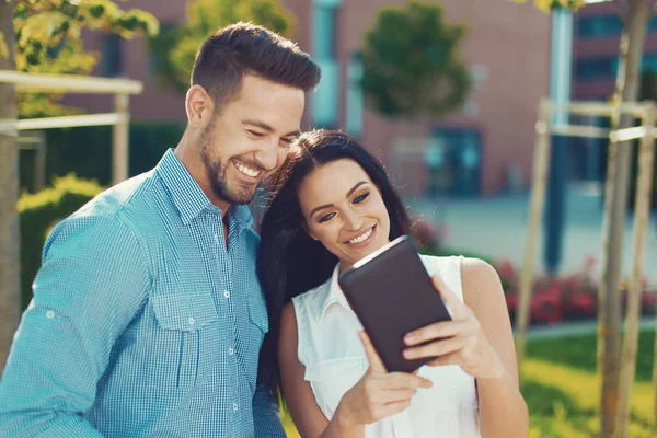 Happy young caucasian couple with tablet outdoors, wireless communication