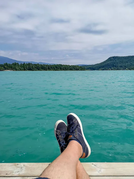 Carefree man with crossed legs sit on pier of lake, relaxation