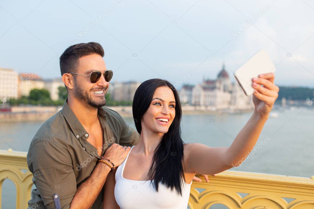 Happy young tourist couple taking selfie in city