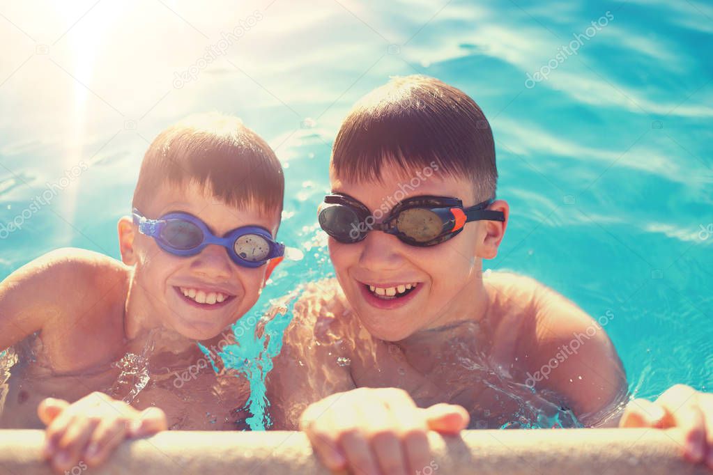 Two young boys holding edge of swimming pool, summer holiday
