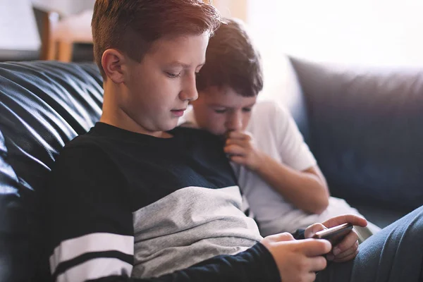 Little boys using smartphone on sofa at home