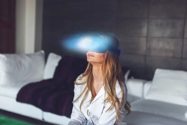 Young blonde woman with VR headset and magical blue light light at home concept, virtual reality