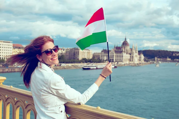 Happy young redhead hungarian woman waving hungarian flag at Bud