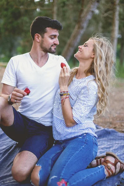 Young woman feeding man with strawberry during picnic