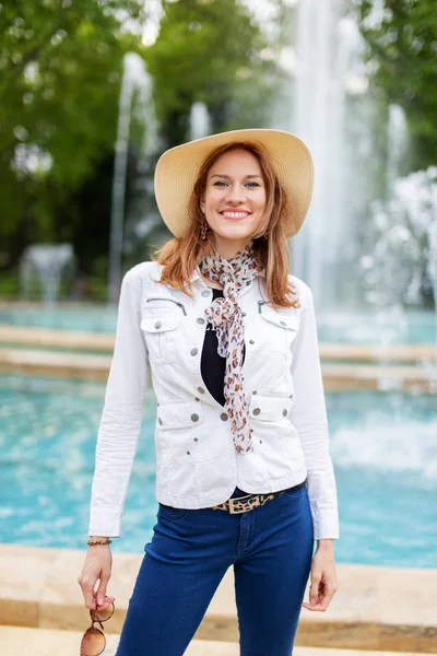 Happy young natural woman in hat at park with fountain