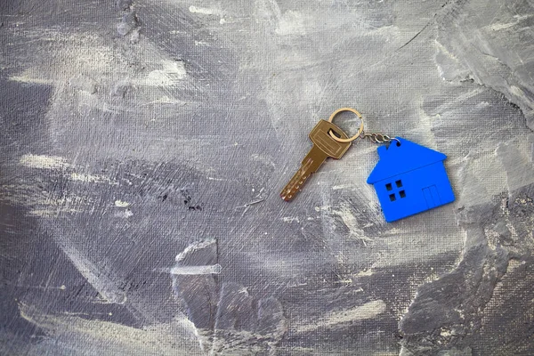 Keys about a charm of the house of blue color on a gray background. Top view. Copy space.