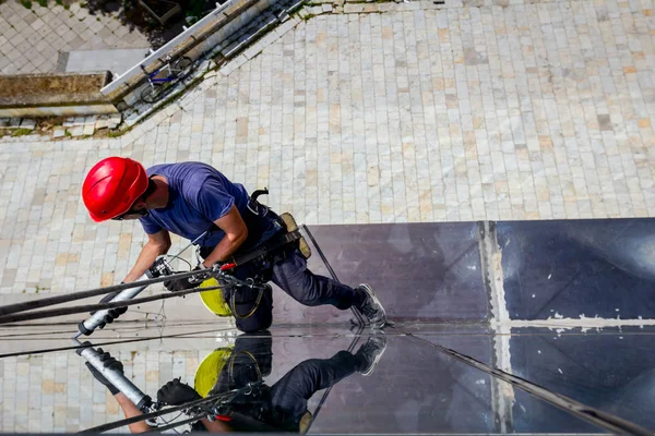 Industrial climber is applying silicone to rubber juncture among building glass facade.