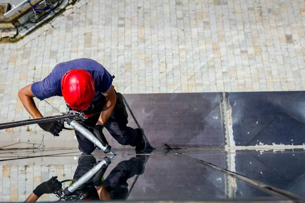 Industrial climber is applying silicone to rubber juncture among building glass facade.