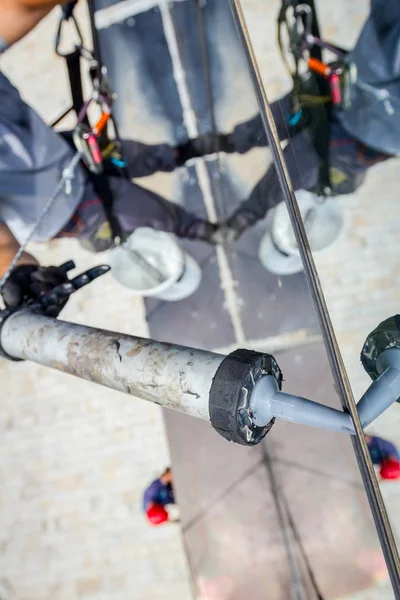 Industrial climber is applying silicone to rubber juncture among building glass facade.