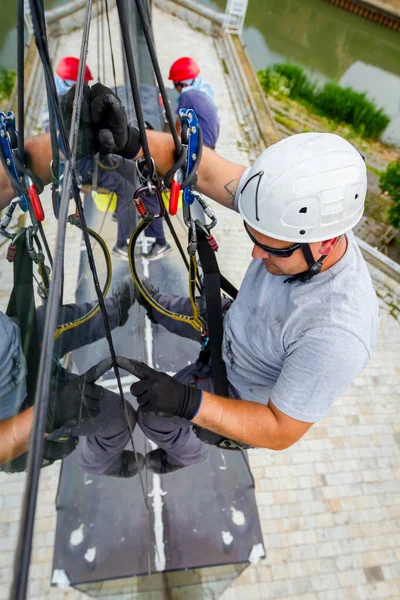 Industrial climbers are applying silicone to rubber juncture among building\'s glass facade.