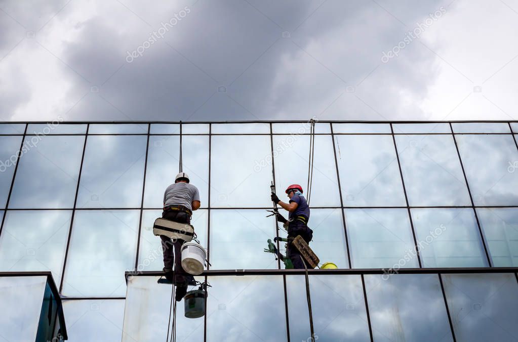 Industrial climbers are applying silicone to rubber juncture among building's glass facade.