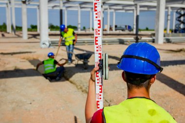 İnşaat işçisi seviyelendirme surveyor, pozisyon, derinlik ölçmek için geodesist yardımcı olmak için çubuk tutuyor.