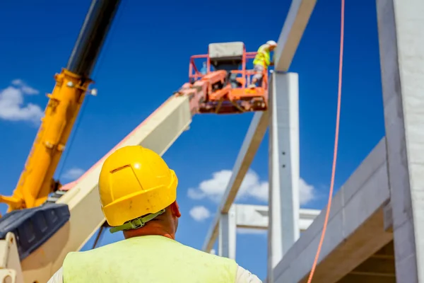 労働者はアセンブリの巨大な建設のためのコンクリートの梁を管理するためにロープで移動式クレーンを支援します — ストック写真