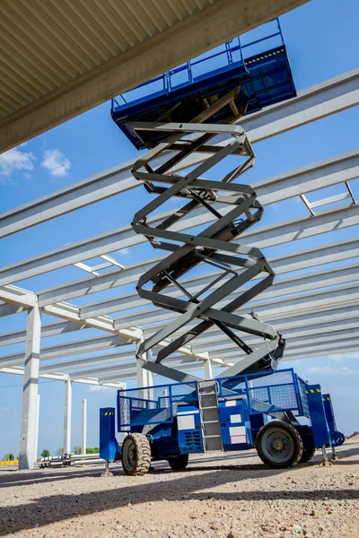 Scissor lift platform with stretched hydraulic system at maximum height range under building skeleton.