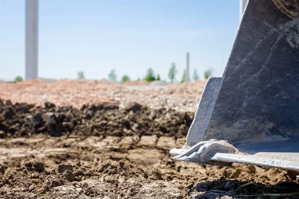 Excavator's tool, bucket, blade, tall concrete pillars are behind at building site.