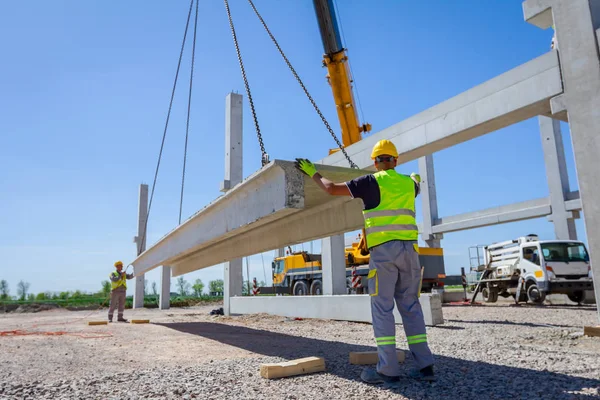 アセンブリの巨大な建設のためのコンクリートの梁を管理する移動式クレーンを支援している労働者 — ストック写真
