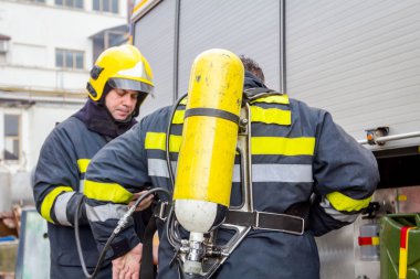 Zrenjanin, Vojvodina, Serbia - March 27, 2018: Firefighter is helping fellow to assembly his gear, keep balance and direction, checking equipment. clipart