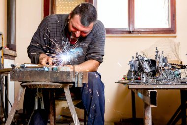 Heykeltraş uygun koruma, silâhsız olmadan derleme metal heykel için ark kaynağı kullanıyor.