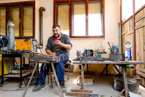 Sculptor is giving stance, attitude to his figures made of metal wire in his workshop.