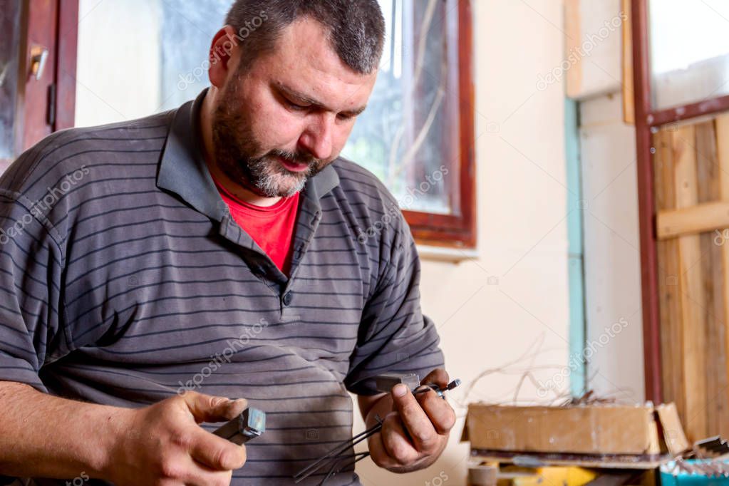 Artist is processing metal with special tools in his hands to curve wire in right shape. 