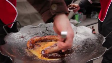 Lezzetli sulu sosis ızgara plakası saplı açma. Metal maşa yardımıyla kaynayan sosis siyah bir mangal üzerinde dönüyor. 