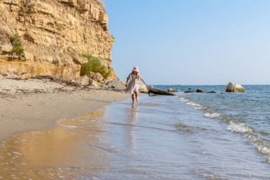 Genç kadın, çocuk şapka ve şirin yazlık elbise çalıştıran ve sığ su, deniz kıyısında.