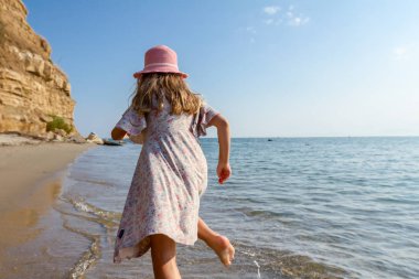 Genç kadın, çocuk şapka ve şirin yazlık elbise çalıştıran ve sığ su, deniz kıyısında.