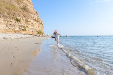 Genç kadın, çocuk şapka ve şirin yazlık elbise çalıştıran ve sığ su, deniz kıyısında.