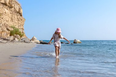 Genç kadın, çocuk şapka ve şirin yazlık elbise çalıştıran ve sığ su, deniz kıyısında.