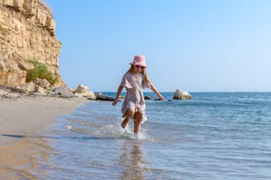 Genç kadın, çocuk şapka ve şirin yazlık elbise çalıştıran ve sığ su, deniz kıyısında.