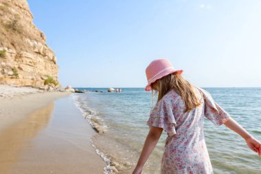 Arkadan genç kadın, çocuk şapka ve çiçek elbise sığ suda, plaj deniz kıyısında şirin yaz görüntüleyin.