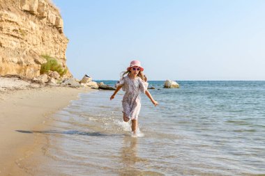 Genç kadın, çocuk şapka ve şirin yazlık elbise çalıştıran ve sığ su, deniz kıyısında.