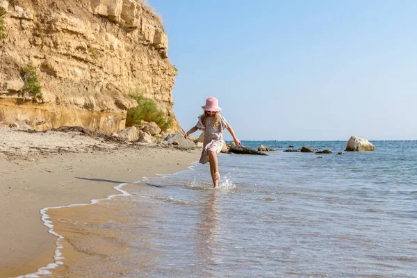 Genç kadın, çocuk şapka ve şirin yazlık elbise çalıştıran ve sığ su, deniz kıyısında.