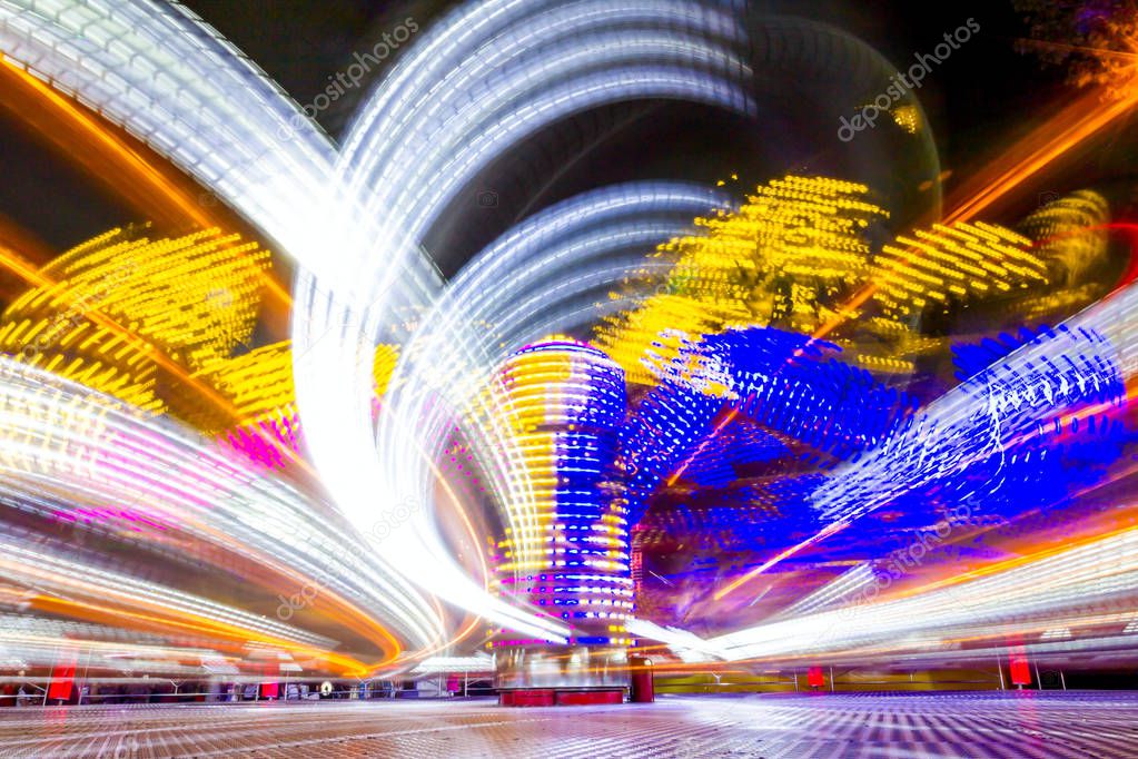 Long exposure of a fast spinning colorful carousel illuminated at night with vivid lightings, funfair ride in Luna Park.