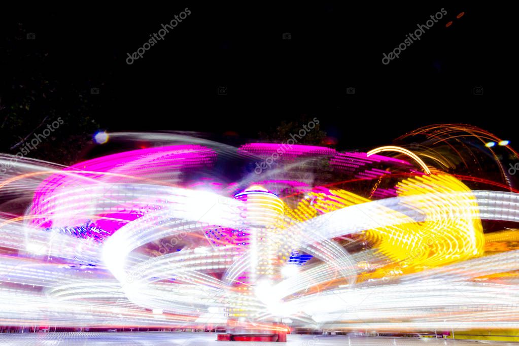 Long exposure of a fast spinning colorful carousel illuminated at night with vivid lightings, funfair ride in Luna Park.