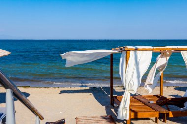 Lüks rahat ahşap pergola şemsiye için beyaz perde ile güneşli kumsalda yerleştirilir.