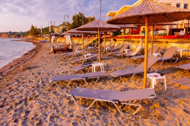 Erken sabah güneş, şafak, Halk Plajı ile thatched şemsiye, şemsiye ve şezlonglar deniz kıyı şeridi boyunca görüntüleyin.