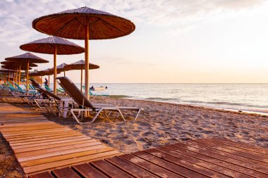 Sabah güneş thatched şemsiye ve şezlonglar ile boş Halk Plajı, ahşap yolda.