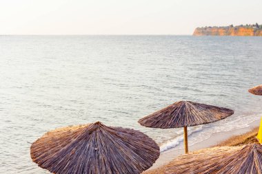 Sabahın erken saatlerinde güneş, şafak, halk plajında sazlı güneş gözlükleri, şemsiyeler ve deniz kıyısı boyunca iskemlelerle.